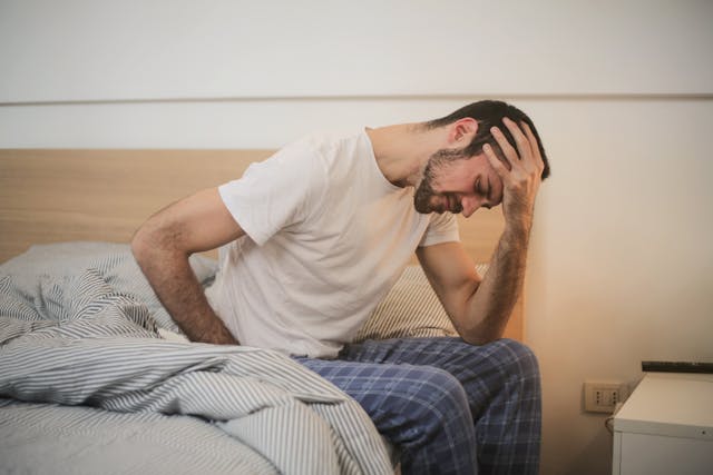 person sitting on a bed and holding their forehead