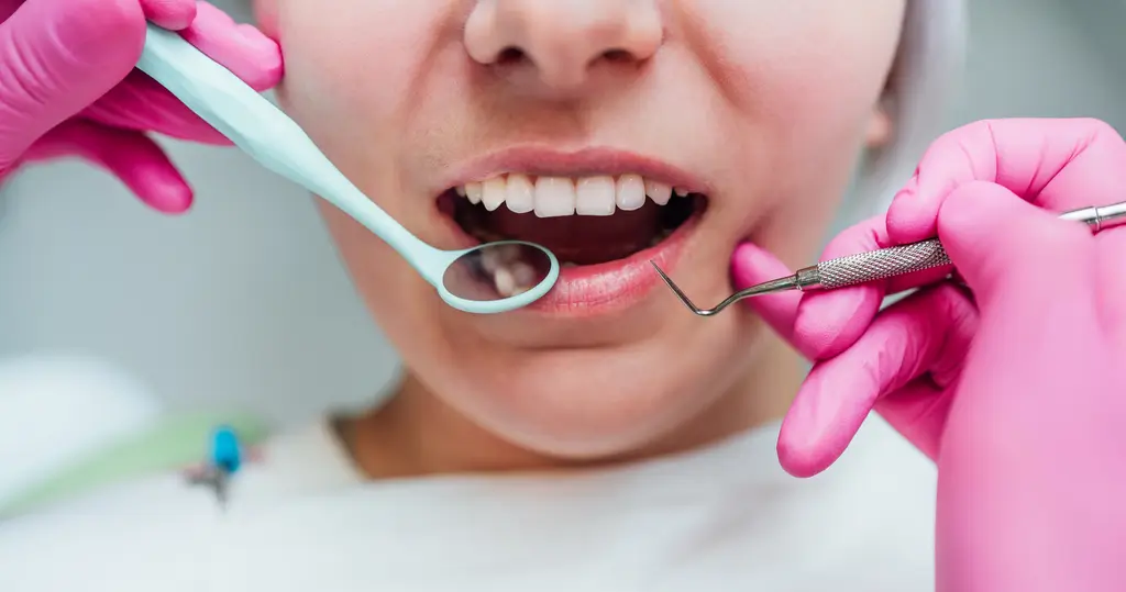 arafed woman in pink gloves holding a toothbrush and a dental instrument