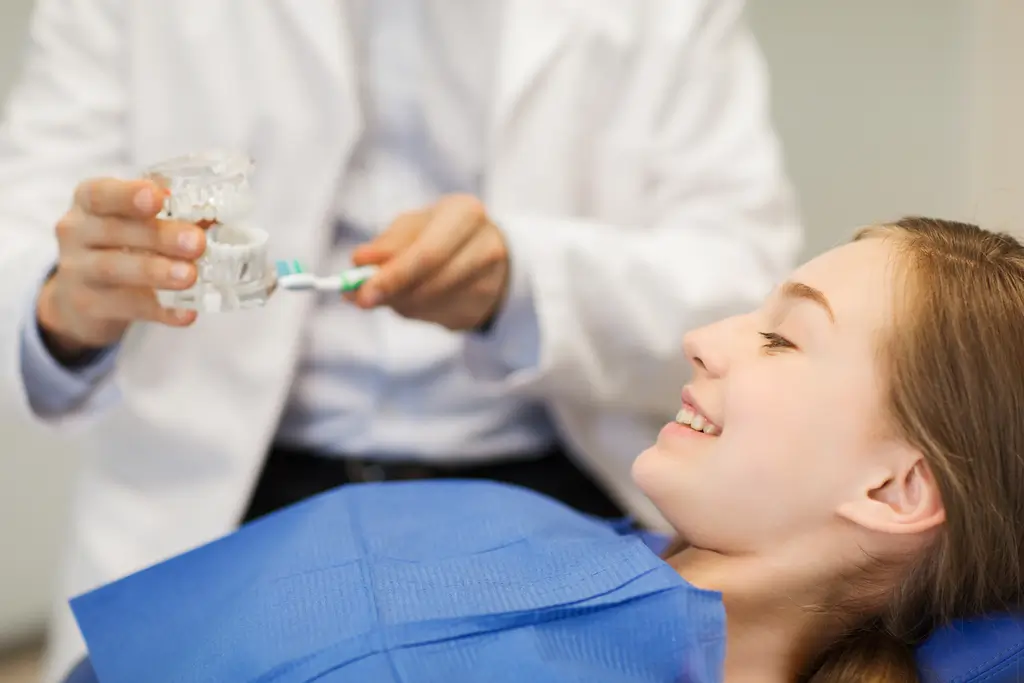 arafed woman in a blue shirt is smiling while a dentist is holding a toothbrush